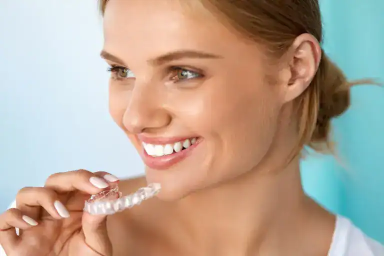 A smiling woman holding a clear dental aligner, showcasing orthodontic treatment at Rincon Dental.