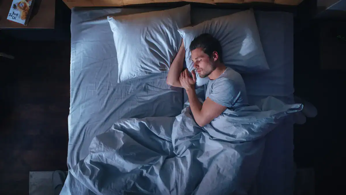 A man sleeping peacefully in bed with gray sheets and pillows.